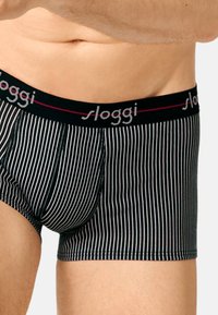 Schwarz-weiße gestreifte Herrenboxershorts mit elastischem Bund, auf dem der Markenname "sloggi" in Grau und Rot abgebildet ist.