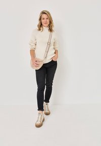Cream ribbed sweater, black fitted jeans, and beige high-top sneakers. Small beige crossbody bag with adjustable strap. Simple design, casual look.
