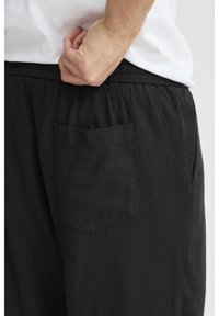 Black linen pants with an elastic waistband, featuring a small, rectangular back pocket and a soft texture. Simple, casual design.