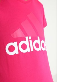 Różowa bawełniana koszulka z krótkim rękawem, z dużym białym logo "adidas" oraz trzema ukośnymi paskami, z okrągłym dekoltem.