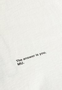 Tissu blanc avec texte noir imprimé disant "The answer is you, MU." dans une police simple sans empattement.