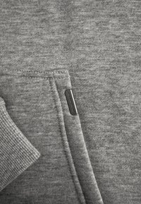 Grijze sweatshirtstof met een gladde textuur, voorzien van een voorkantzak en een klein zwart label dat in de naad is genaaid.