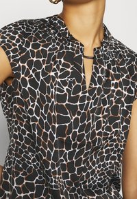 Blusa sin mangas negra con estampado de jirafa en patrones blancos y marrones, con una tapeta parcial y una textura sutil.