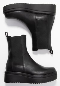 Black leather ankle boots with elastic side panels, a textured sole, and pull tabs. Features a smooth finish and low wedge platform.