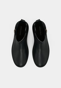 Par črnih usnjenih gležnjakov s stranskimi sponkami, prikazanih s ptičje perspektive na beli podlagi.