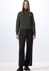 Maglione a collo alto in maglia a coste verde scuro abbinato a pantaloni cargo neri a gamba larga e scarpe nere chunky. Texture liscia, stile casual.