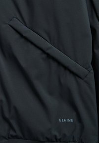 Zwarte outerwear heeft een gladde textuur, zijzakken, een geribde zoom en een klein "ELVINE" logo aan de onderkant.
