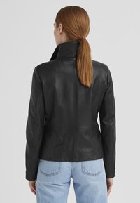 Schwarze Lederjacke mit taillierter Passform, Stehkragen und glatter Textur. Der Rücken weist vertikale Nähte auf und hat eine schlanke Silhouette.