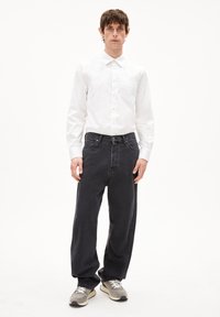 Weißes Hemd mit Knopfleiste, dunkelgraue lässige Jeans und graue Sneakers mit weißen Schnürsenkeln. Schlicher Hintergrund, neutrale Farben.