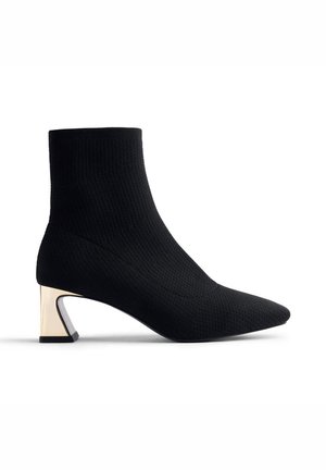 Botte de cheville en tricot noir avec un bout pointu et un talon en bloc triangulaire métallique. Texture lisse avec une silhouette ajustée.