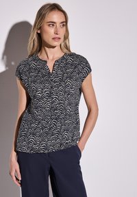 Top blu navy a maniche corte con motivo a onde in crema, colletto rotondo e vestibilità comoda. Tessuto liscio, dettagli minimi.