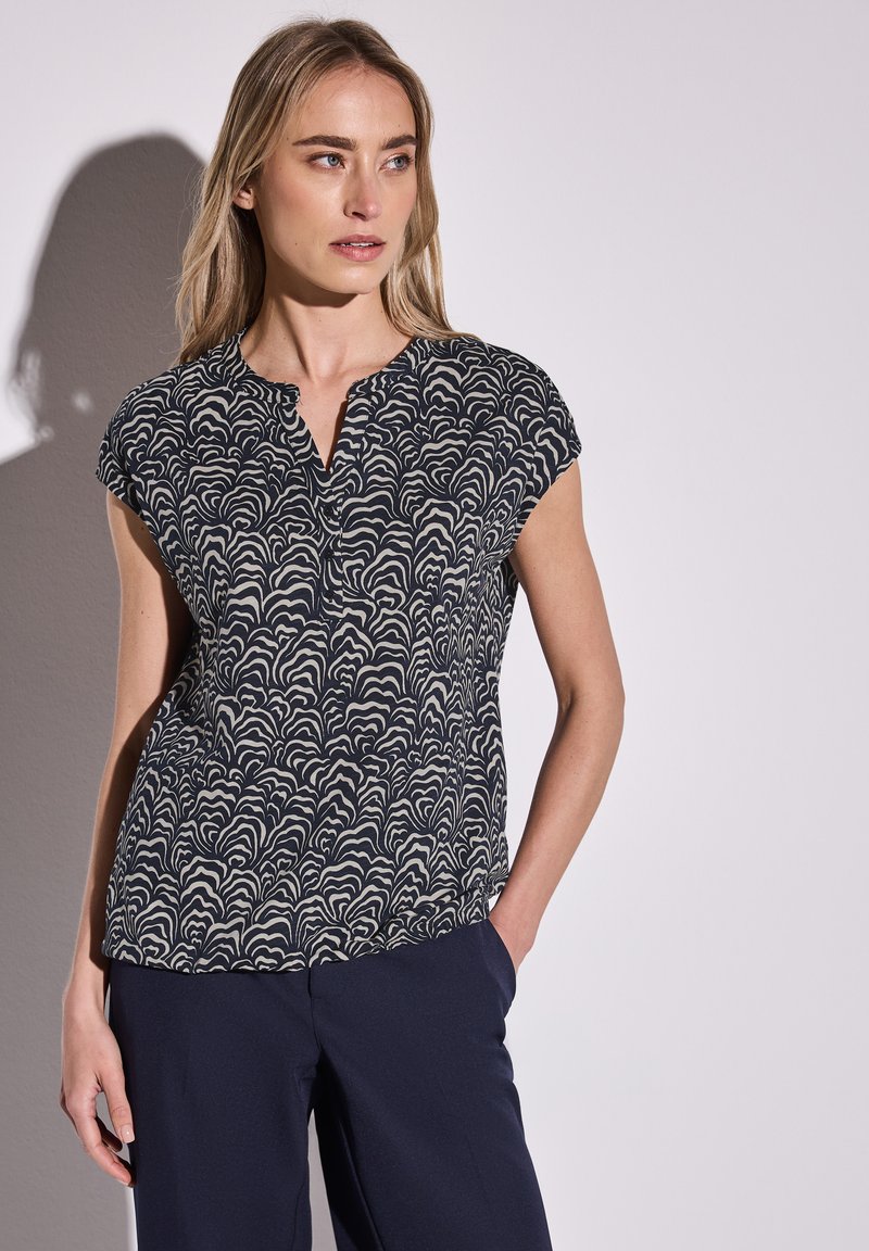 Top blu navy a maniche corte con motivo a onde in crema, colletto rotondo e vestibilità comoda. Tessuto liscio, dettagli minimi.