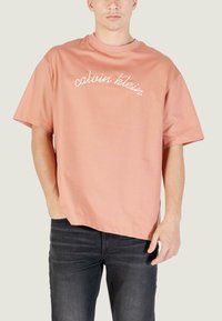 T-shirt di cotone rosa chiaro con maniche corte e scollo rotondo, con logo bianco in corsivo sul davanti. Vestibilità comoda.