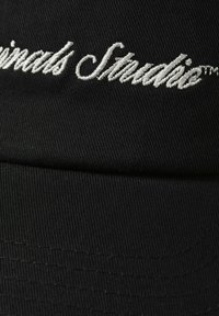 Zwarte pet van textiel met structuur, voorzien van witte geborduurde tekst die "Originals Studio" zegt. Vlakke klep en gestructureerd ontwerp.