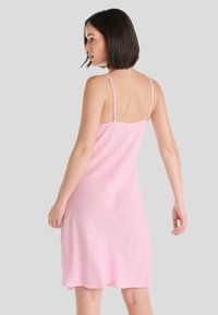 Vestido sin mangas rosa con tirantes finos, una silueta fluida y un sutil patrón geométrico. Tejido suave con una textura lisa.