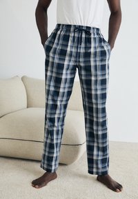 Pantalons de pyjama à carreaux navy avec une taille élastique, un cordon de serrage réglable, des poches latérales et une texture de tissu douce et lisse.
