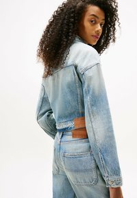 Giacca di denim blu chiaro con taglio classico, caratterizzata da toppe sulla schiena, cuciture a contrasto e dettagli con bottoni in metallo.