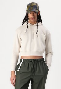Beige cropped hoodie with drawstring, white logo; green lightweight pants with elastic waist and side stripe; green plaid cap.