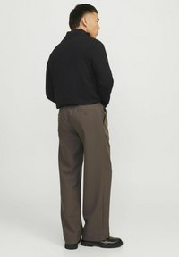 Melna adīta pulovera ar augstu apkakli, apvienota ar brūnām platām biksēm ar aizmugurējo kabatu detaļu un melnām kurpēm.