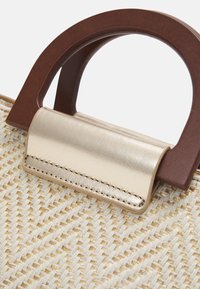 Woven handbag with a beige body, brown circular handle, and gold accents. Features a textured exterior and a flat gold leather flap closure.