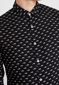 Camisa negra con pequeño estampado de animales en beige, que presenta un cuello clásico y botones blancos. Tejido ligero con una textura suave.