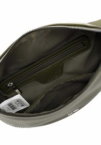 Interno della borsa a tracolla verde oliva con tasca con zip in pelle texturizzata, fodera liscia e zip argentata. Il marchio è visibile alla base.