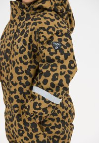 Barn iført brun og sort leopardmønstret jakke med hætte, refleksstribe på ærmet og "ZIGZAG" logo-lap på overarmen.