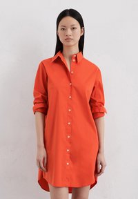 Robe chemise en coton rouge avec un devant boutonné, des manches retroussables et un ourlet incurvé, dotée de boutons blancs et d'un col classique.