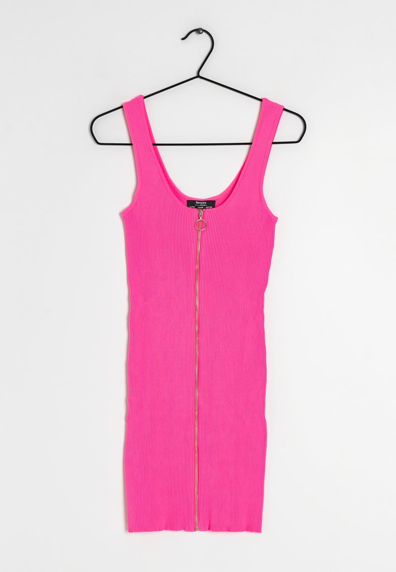Aangemeten roze geribbelde jurk met brede banden, voorzien van een gouden rits aan de voorkant en een split aan de onderkant. Hangend aan een zwarte haak.