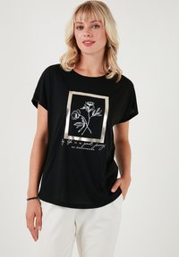 Zwarte T-shirt met korte mouwen, voorzien van een bloemenafbeelding in een gouden omlijsting en witte tekst. Gemaakt van zachte stof met een relaxte pasvorm.