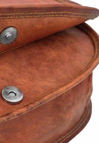 Kulatá hnědá kožená taška s viditelným šitím a kovovým zapínáním, které ukazuje hladkou strukturu a mírně opotřebovaný povrch.