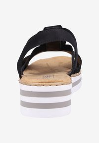 Sandale noire avec deux sangles, semelle intérieure rembourrée et une épaisse semelle en plateforme blanche avec des rayures grises. Matériau en suède doux, design léger.