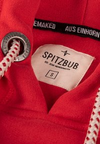 Rode sweatshirt stof met een label waarop "SPITZBUB" staat. Bevat een zilveren oogje met een witte trekkoord. Het label vermeldt maat "S" en merkinformatie.