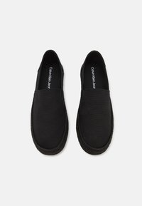 Sorte slip-on sko med overdel i kanvas og flettet taustøvel. Har enkelt design, rund tå og merket innersåle.