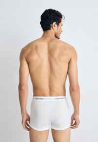 Boxer-briefs blancs en coton avec un ajustement près du corps, dotés d'une taille étiquetée "Calvin Klein" en gris et noir. Tissu texturé, design minimaliste.