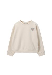 Sweatshirt couleur crème avec un col rond, des épaules tombantes et un patch en forme de cœur avec un motif floral sur la poitrine gauche. Texture douce.