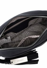 Melna perforēta ādas rokassomiņa ar sudraba rāvējslēdzēju. Iekšpusē ir gaismas raksta auduma oderējums un papildu rāvējslēdzēja kabata.