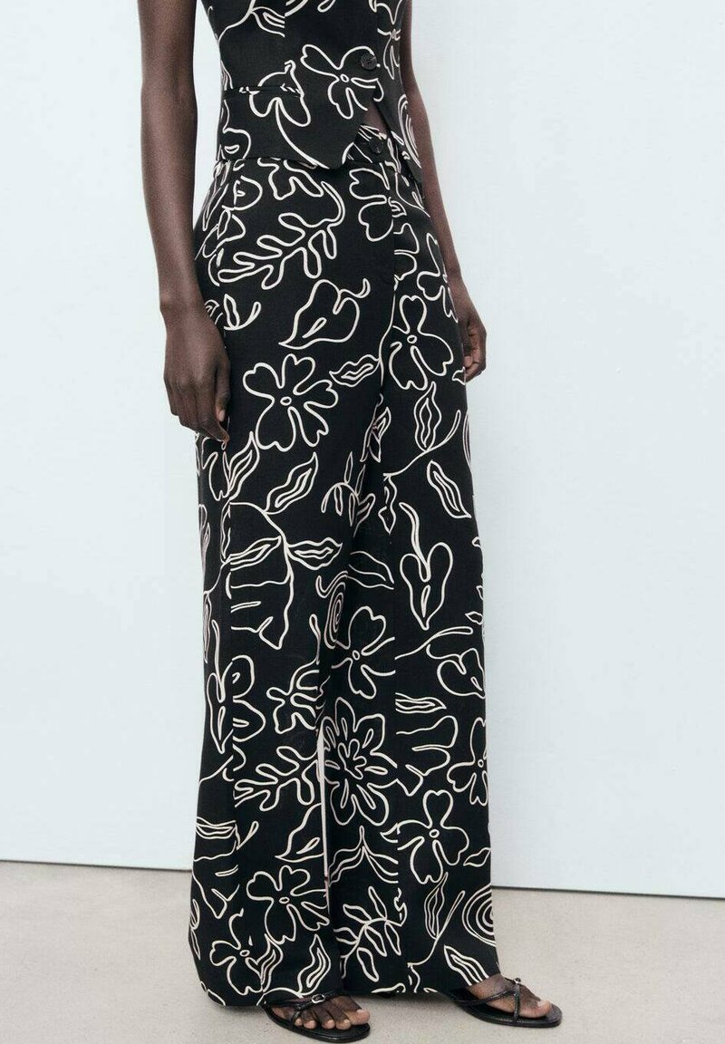 Pantalons larges noirs avec un motif floral crème, fabriqués dans un tissu léger, avec une texture douce et une coupe décontractée.