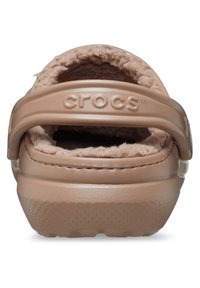 Klumpy Crocs w miękkim odcieniu beżu, z puszystą wewnętrzną wyściółką, elastycznym paskiem na pięcie i teksturowaną podeszwą dla lepszej przyczepności.