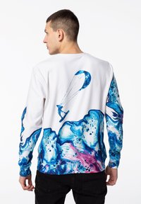 Bílé mikina s dlouhým rukávem, která má modro-růžový abstraktní vlnový design a grafiku kitesurfera na zádech.