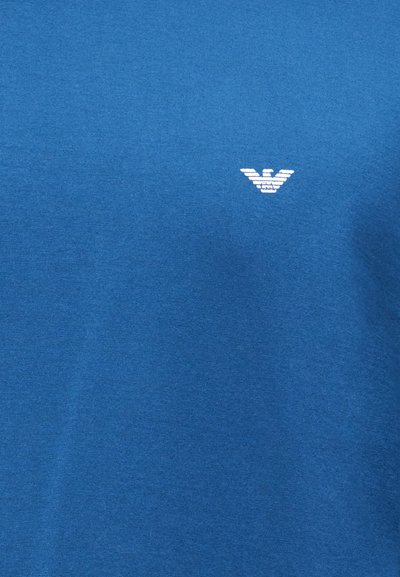 Μπλε βαμβακερό t-shirt με μικρό λευκό λογότυπο αετού στο στήθος, με λεία υφή και κλασικό στρογγυλό λαιμόκοψη.