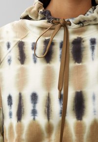 Felpa tie-dye nei colori crema, marrone e blu navy. Realizzata in tessuto morbido, con cappuccio regolabile e lacci per una vestibilità personalizzata.