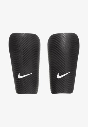 Protège-tibias noirs Nike avec une surface texturée et nervurée, et un logo Nike blanc bien visible sur chaque protection, conçus pour un usage athlétique.