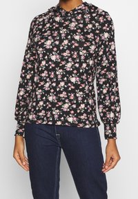 Sweat à capuche noir à manches longues avec un imprimé floral rose et blanc, doté d'une capuche à cordon et de poignets élastiques. Tissu doux, design décontracté.