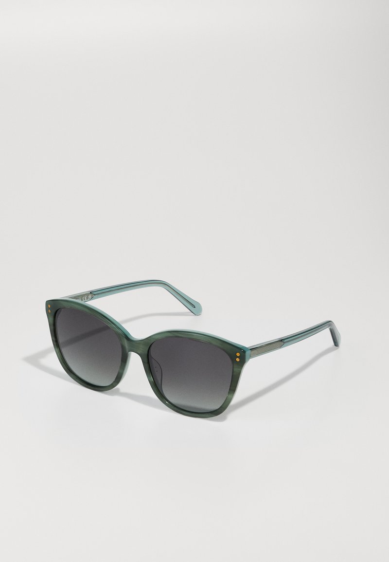 Groen getinte oversized zonnebril met gradient donkere lenzen, glanzend plastic frame en drie kleine gouden stippen op de buitenranden.