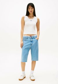 Witte mouwloze top, lichtblauwe denim shorts en witte sneakers met bruine zolen. Zichtbaar merklogo op de tailleband van de shorts. Gladde textuur.