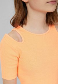 Geribbeld, korteblauwe top in fel oranje met schouderuitsparingen. Zachte textuur en strakke pasvorm benadrukken de halslijn en mouwen.