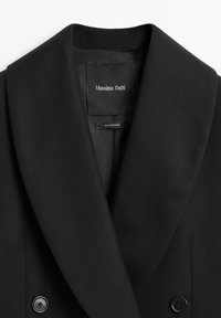 Černý dvojřadý kabát z vlněné směsi se širokým klopovým límcem, s dvěma černými knoflíky a štítkem s nápisem "Massimo Dutti" uvnitř.