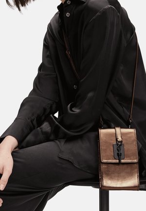 Sac bandoulière métallique bronze avec rabat, forme rectangulaire, ferrures noires et bandoulière réglable. Texture lisse, design minimaliste.