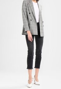 Blazer grigio a quadri doppiopetto, top bianco, jeans neri con dettagli in perle e scarpe con tacco bianche. Vestibilità sartoriale e lunghezza cropped.
